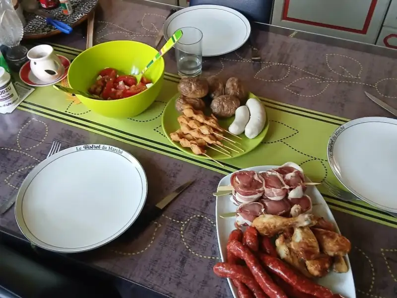 烧烤餐桌上的生鸡肉串，旁边有香肠、鸡腿、培根肉卷和番茄沙拉